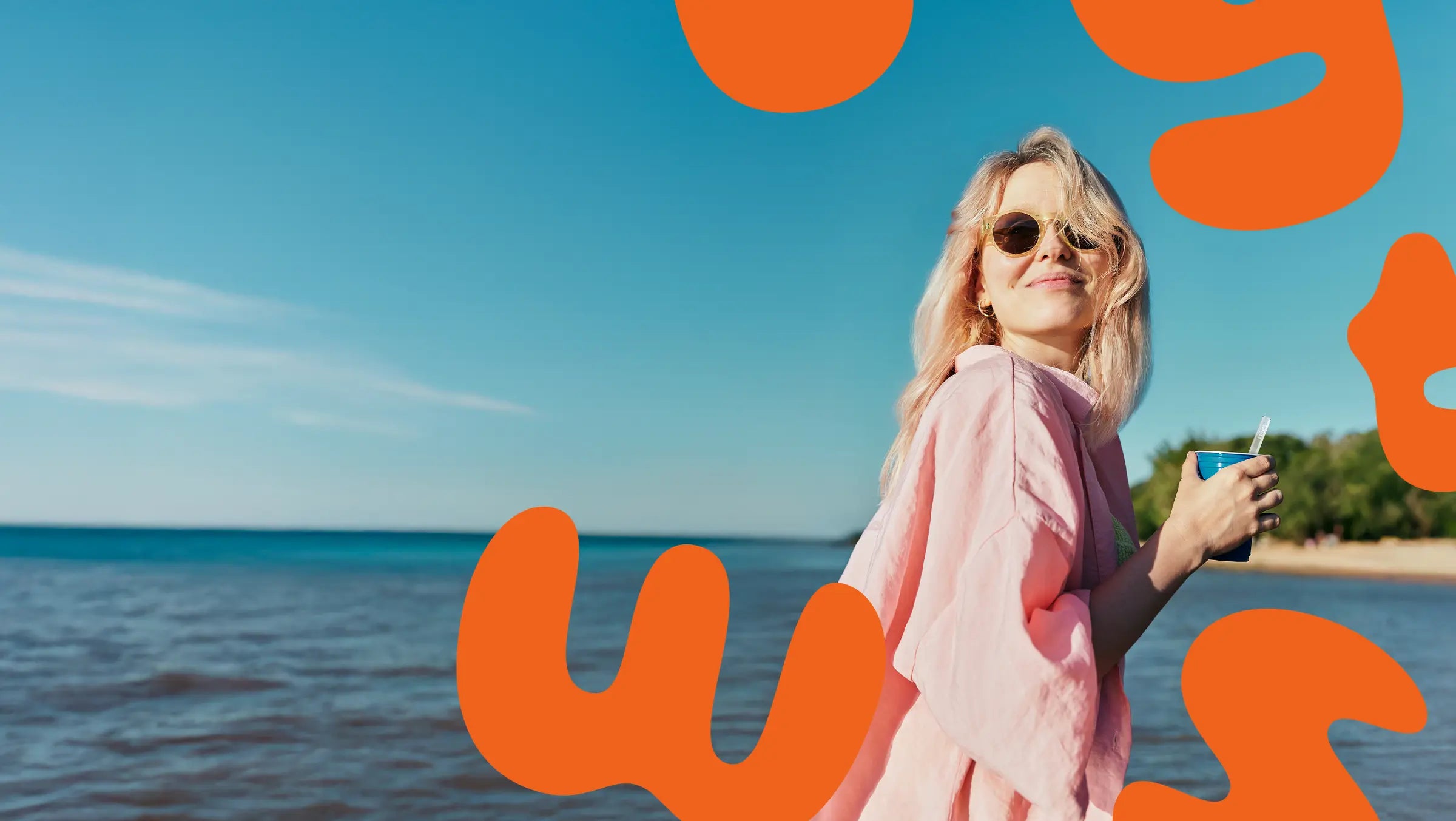 Woman in a pink dress holding a cup with a Twyst straw standing by the ocean with large orange letters overlayed.